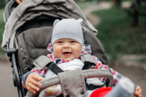Baby boy in warm colorful knitted jacket sitting in modern stroller on a walk in a park. Child in buggy. Little kid in a pushchair. Traveling with young kids. Transportation for family with infant.