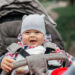 Baby boy in warm colorful knitted jacket sitting in modern stroller on a walk in a park. Child in buggy. Little kid in a pushchair. Traveling with young kids. Transportation for family with infant.